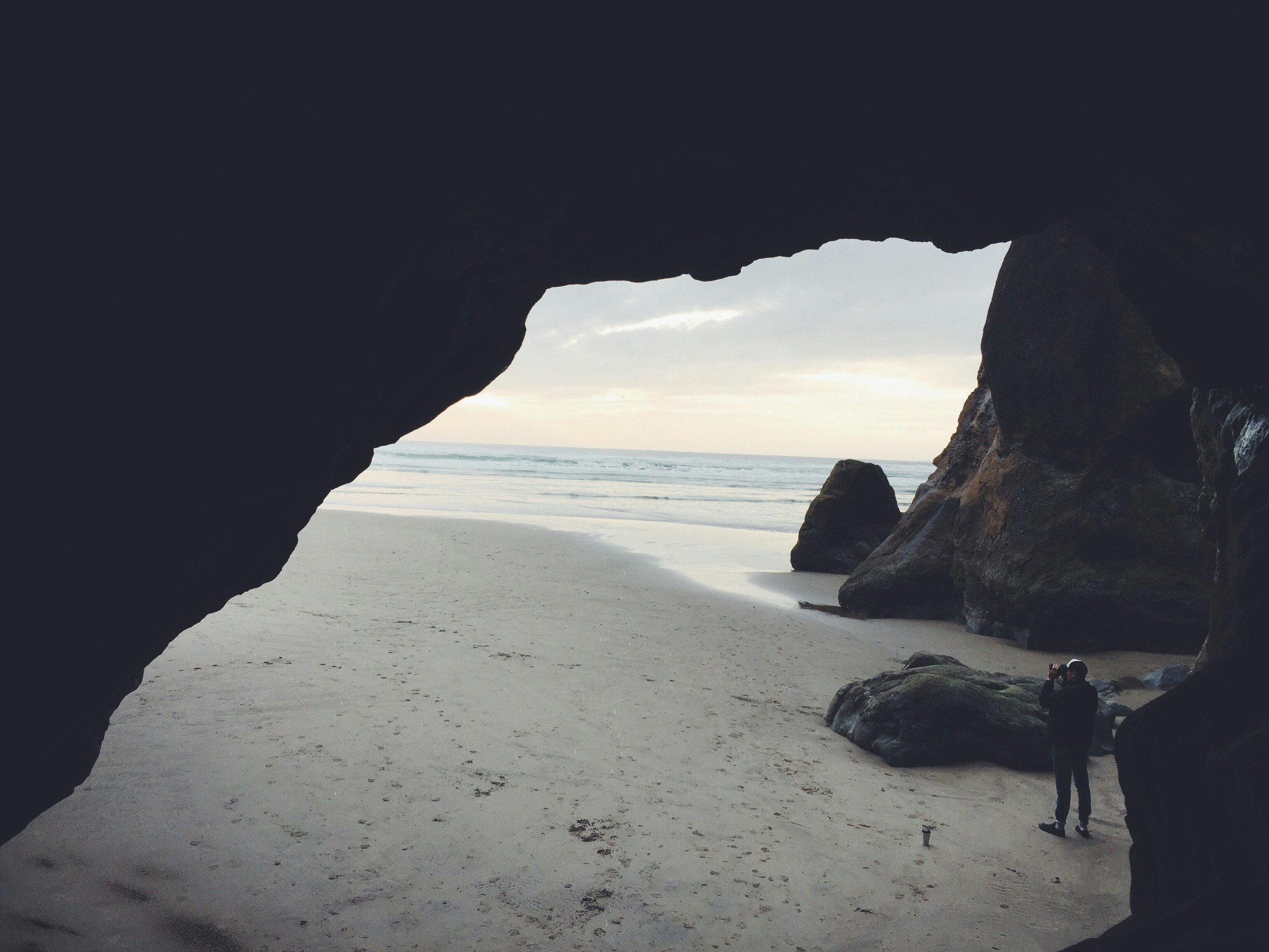 person taking picture beside cave